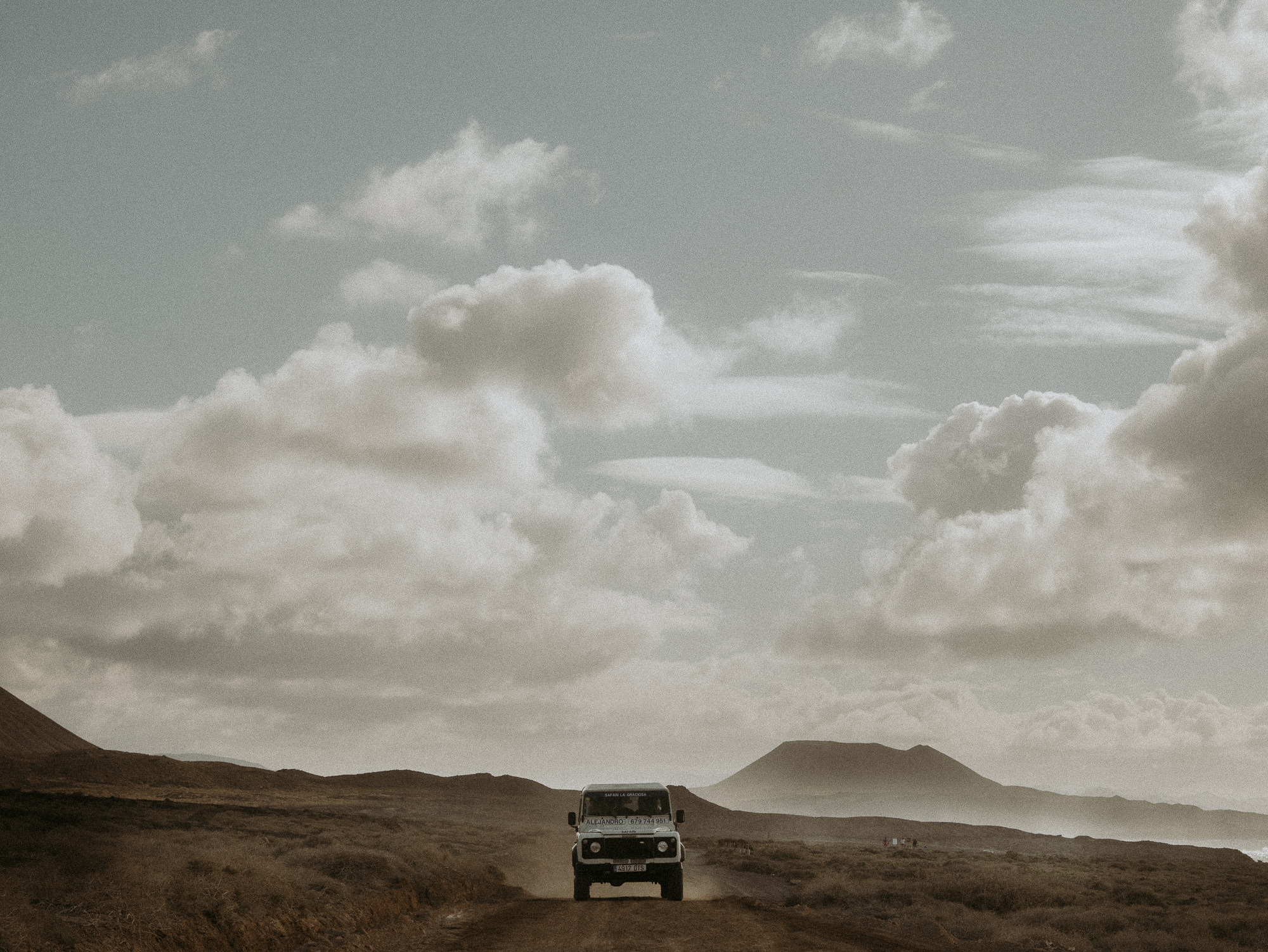 Land Rover Defender drives across desert road on the island of La Graciosa.