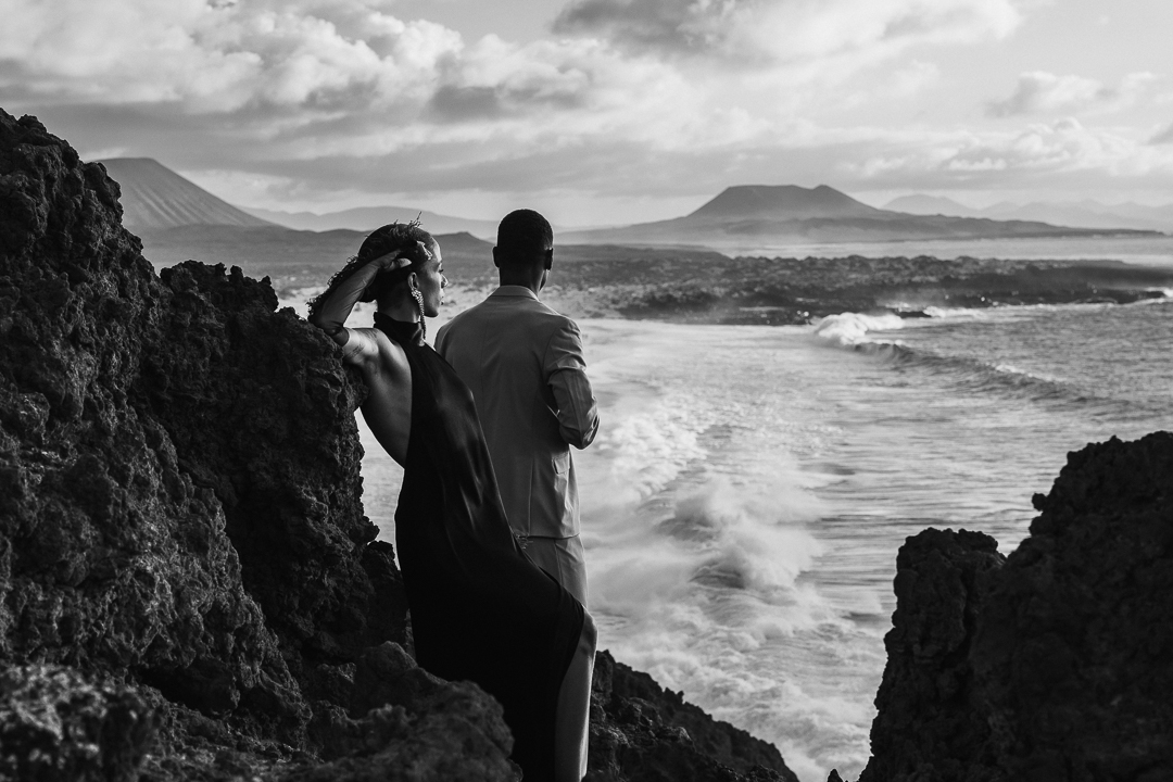 Couple in dress and suit look out across incrdebile ocean view at sunset at Plays de la Conchas. 